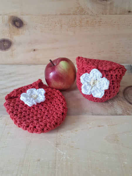 Red crochet pouch sits on barn wood beside apple. 5 petal flower applique button.